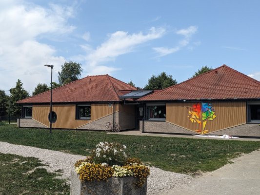 Bâtiment avec toits rouges, murs en bois, panneaux solaires, graffiti, vélo, réverbère, fleurs.