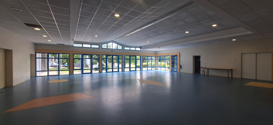 Salle vide avec grandes fenêtres, portes et taches au sol.