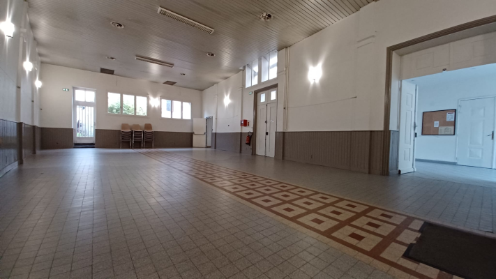 Salle vide avec sol carrelé, murs en bois et blanc, portes et fenêtres. Éclairage suspendu au plafond.