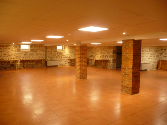 Salle avec murs de pierre, colonnes de brique, sol carrelé, éclairage au plafond.