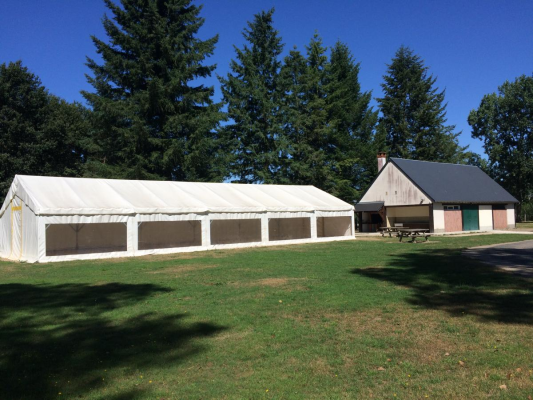 Tente de réception blanche près d'un bâtiment en bois, avec des arbres en arrière-plan.