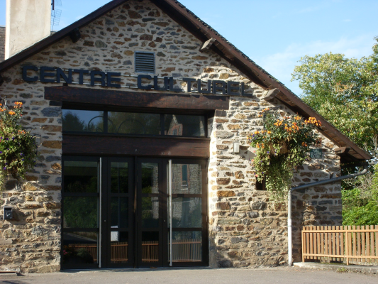 Bâtiment en pierre avec entrée vitrée, enseigne "Centre Culturel" et fleurs suspendues.