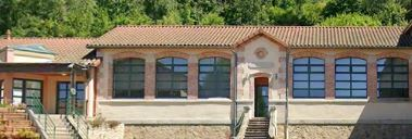 Bâtiment avec toiture en tuiles, grandes fenêtres, porte d'entrée centrale et rampe d'accès.