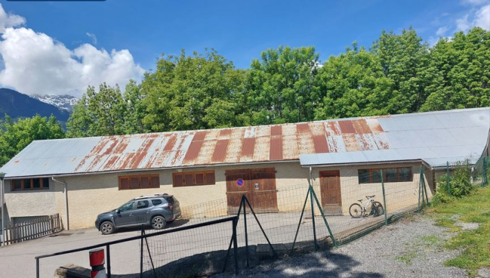 Bâtiment industriel avec toit en métal, voiture, vélo, grillage.