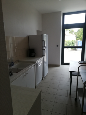 Cuisine avec évier, réfrigérateur, four, micro-ondes, table et chaises. Porte vitrée menant à l'extérieur. Carrelage au sol.