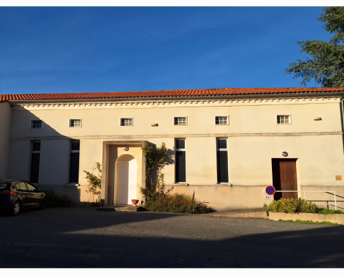 Bâtiment avec toiture rouge, murs beiges, fenêtres, portes, voiture et panneau de stationnement interdit.