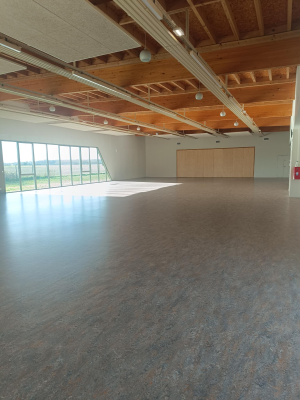 Salle spacieuse avec parquet, grandes fenêtres, plafond en bois, porte en bois et extincteur.