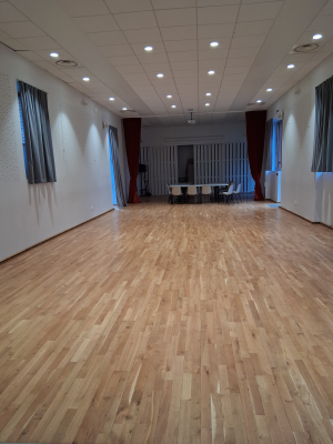 Salle vide avec parquet, tables, chaises et rideaux.