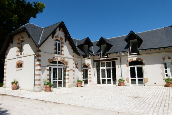 Bâtiment à deux étages avec pignons, briques apparentes, portes vitrées et pots de fleurs.