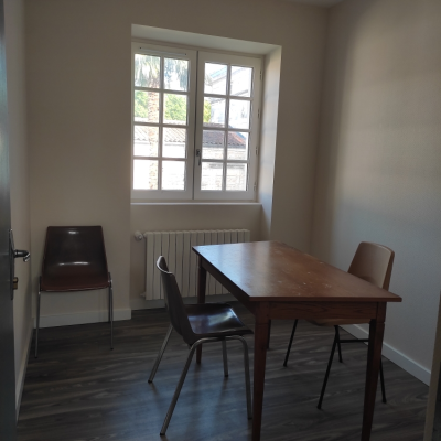 Pièce avec table, quatre chaises, radiateur et fenêtre.