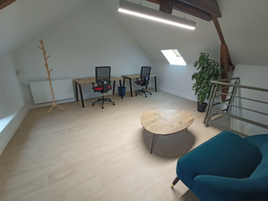 Bureau avec tables, chaises, ordinateurs, porte-manteau, table basse, plante.