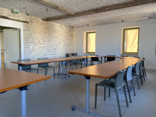 Salle de classe avec tables, chaises, tableau blanc et fenêtres.