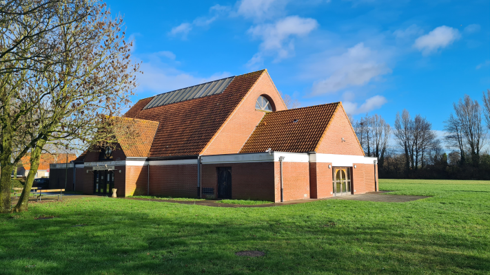 Bâtiment en briques avec toit en tuiles, pelouse et arbres.
