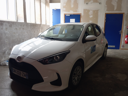 Voiture blanche garée dans un garage avec portes bleues et extincteurs.