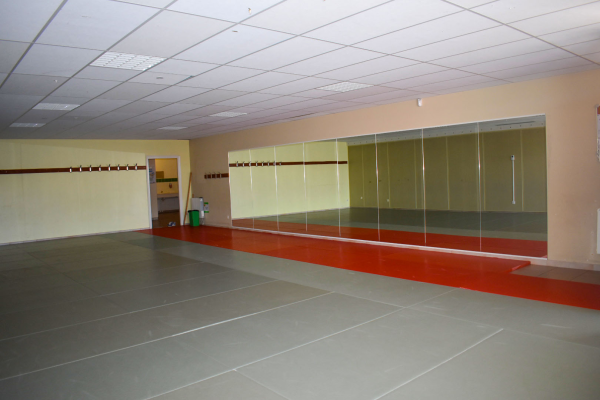 Salle vide avec miroirs, sol carrelé, porte et poubelle verte.