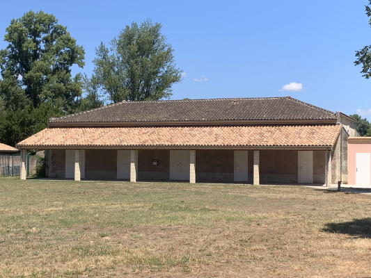 Bâtiment avec toit en tuiles, colonnes et portes ouvertes. Pelouse devant.