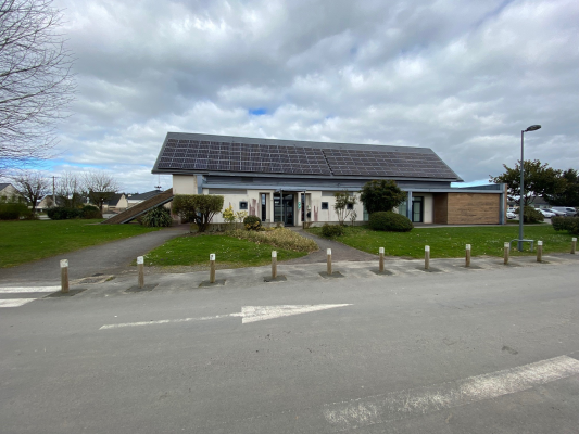 Bâtiment avec panneaux solaires, allée et parking.