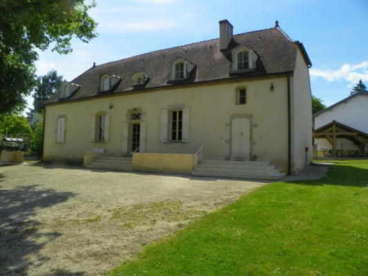 Maison à deux étages avec toit en ardoise, fenêtres à volets et porte d'entrée. Escaliers extérieurs et jardin.