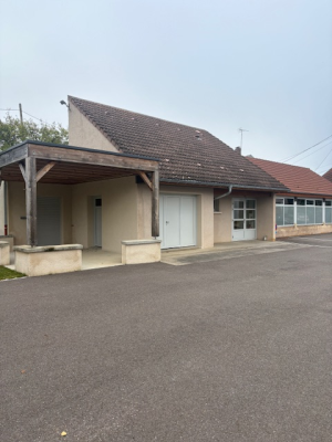 Bâtiment avec toit en tuiles, porte blanche, fenêtres et parking.