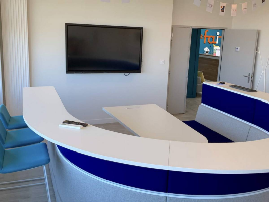 Salle de réunion avec table, chaises, écran et porte avec logo.