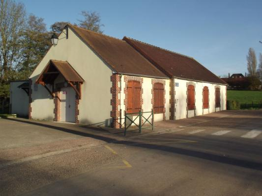 Bâtiment avec toit en tuiles rouges, murs blancs, volets en bois et porte d'entrée.