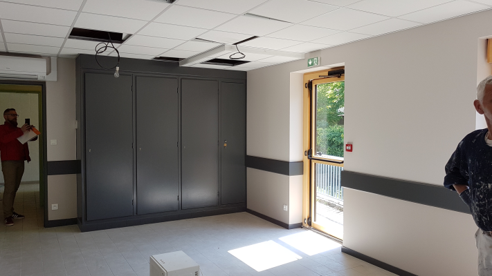 Pièce avec armoires, porte, personne à droite, personne prenant une photo à gauche, boîte au sol.