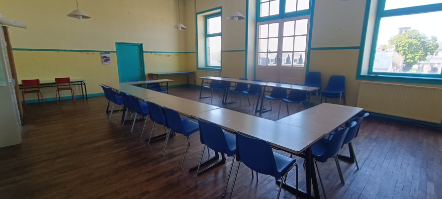 Salle avec tables, chaises, fenêtres et portes.
