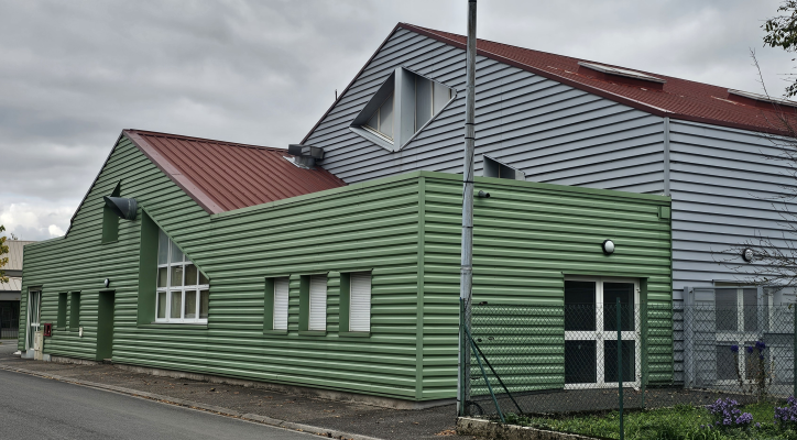 Bâtiment industriel avec façade en bois vert et toit rouge.