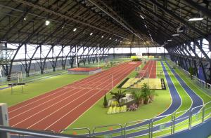 Stade intérieur avec piste d'athlétisme, gradins et équipements sportifs.