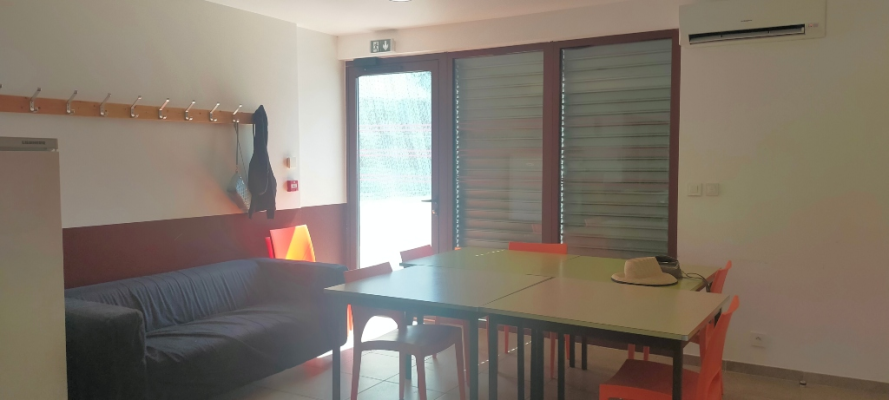 Pièce avec canapé, table, chaises, porte-manteau, climatiseur et porte vitrée.