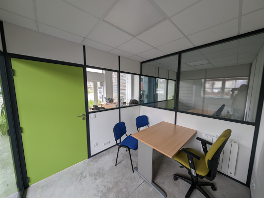 Bureau avec table, quatre chaises, mur vert, cloison vitrée, vue sur open-space.