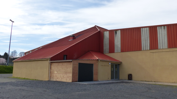 Bâtiment industriel avec toit rouge, murs beiges et bruns, porte de garage et entrée principale.