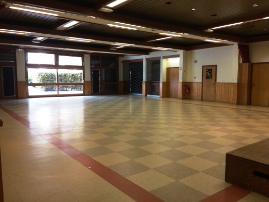 Salle vide avec carrelage en damier, portes et grande fenêtre.