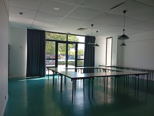 Salle avec tables, chaises, luminaires suspendus et grandes fenêtres.