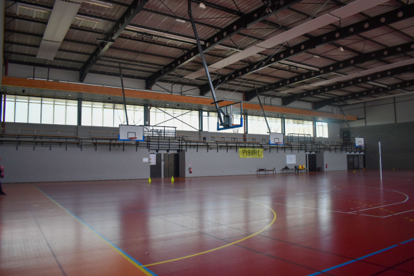 Gymnase avec panier de basket, panneaux de score, et lignes de terrain.