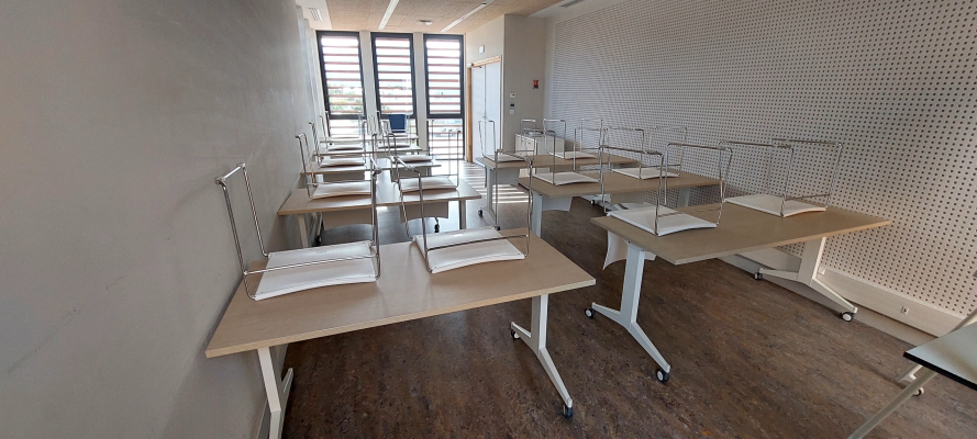 Salle de classe avec bureaux, chaises et tableau blanc.