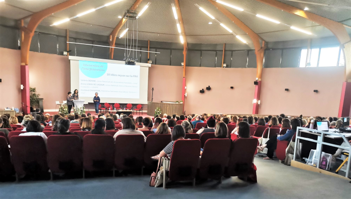 Salle de conférence avec écran, podium, chaises, projecteur et public.