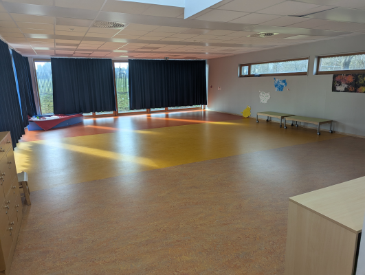 Salle avec sol en parquet, fenêtres, bancs, et tableau.