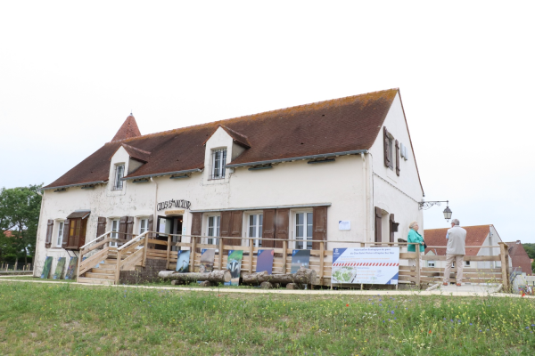 Bâtiment avec toit en pente, portes en bois, fenêtres, panneau d'affichage et clôture.