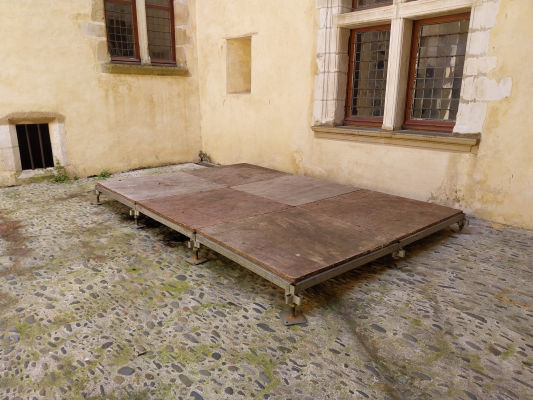 Table en bois sur sol pavé devant un mur avec fenêtres.