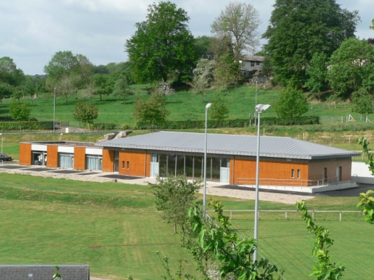 Bâtiment orange avec toit gris, situé dans un environnement vert et arboré.