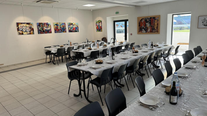 Salle de repas avec tables, chaises, verres, assiettes, couverts et bouteilles.