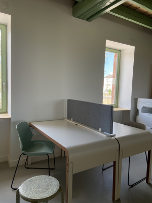 Bureau avec séparateurs, deux chaises vertes et tabouret circulaire.