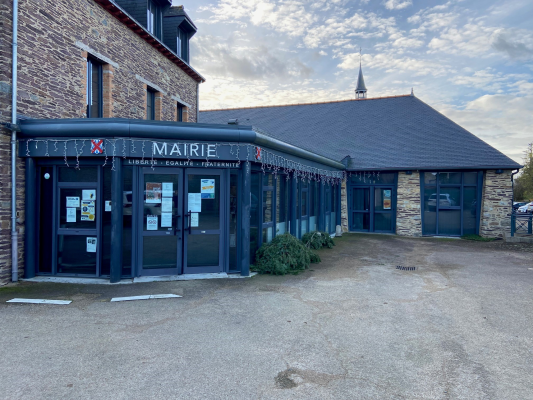Bâtiment de mairie avec façade en pierre et entrées vitrées, parking devant.