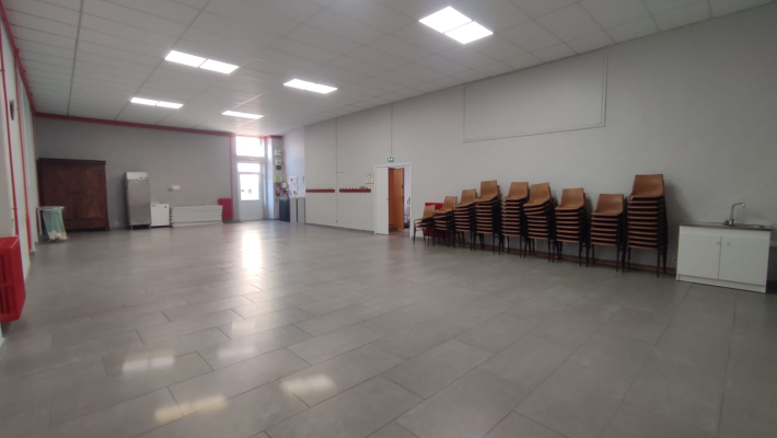 Salle vide avec chaises empilées, évier et meuble de rangement.