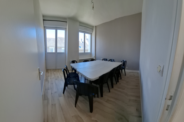 Salle avec table, chaises, portes vitrées et parquet.