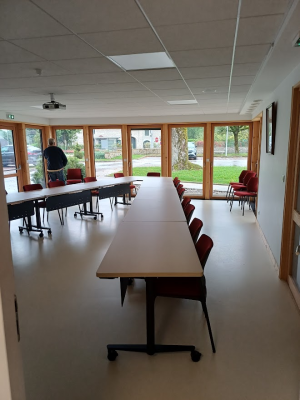 Salle avec tables, chaises, vidéo projecteur, portes vitrées.