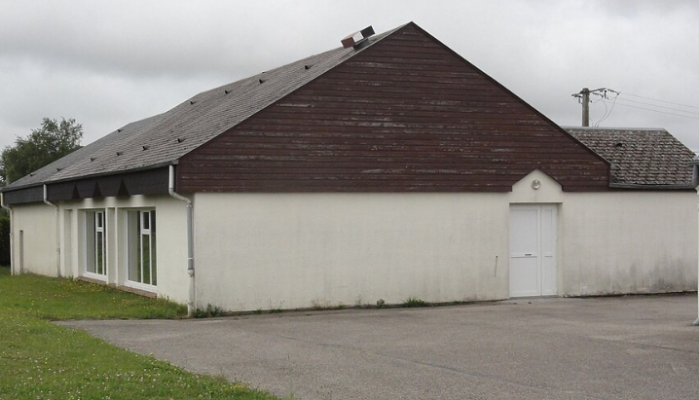 Bâtiment avec toit en pente, murs blancs, fenêtres et porte.