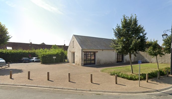 Bâtiment avec parking, buissons, arbre et lampadaire.
