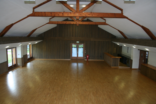 Salle vide avec plancher en bois, poutres apparentes, fenêtres, portes.